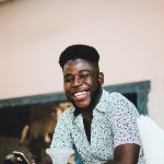 Happy African American man smiling while holding a phone and enjoying coffee indoors.